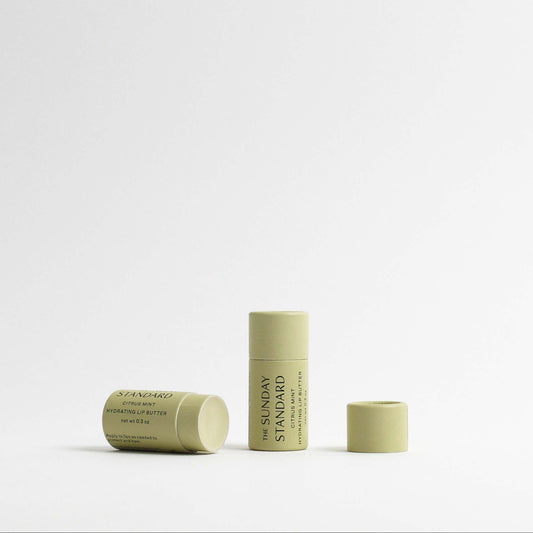 Two tubes of The Sunday Standard's Citrus Mint Hydrating Lip Butter, shown open with a creamy texture.