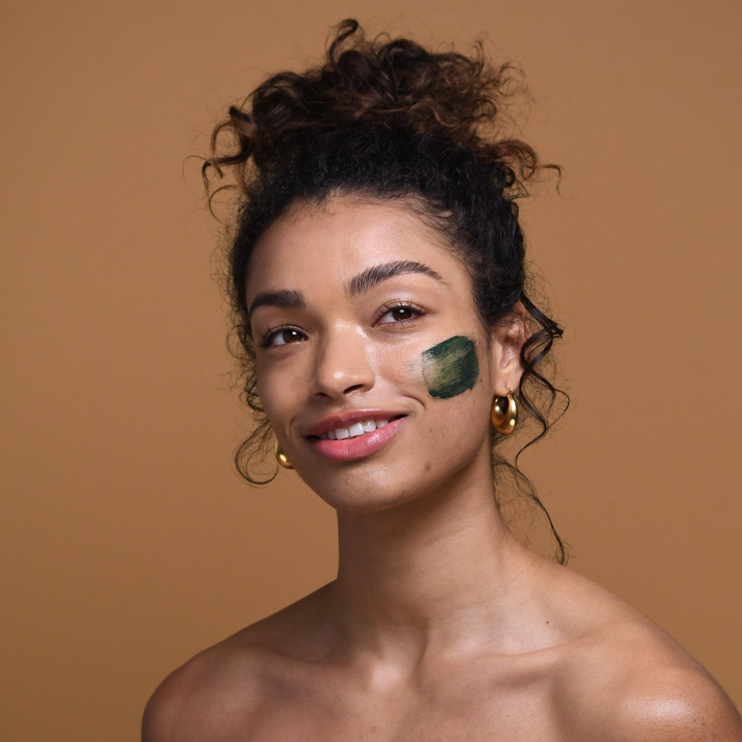 a photo of a young woman with a swatch of dark green mask on her cheek